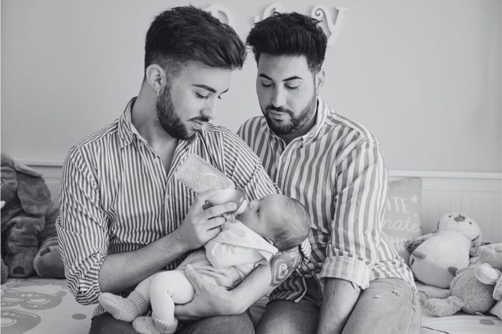 Two fathers feeding their baby at home