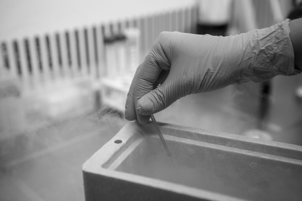 A gloved hand carefully retrieving a vial from a cryogenic storage container with visible liquid nitrogen vapor