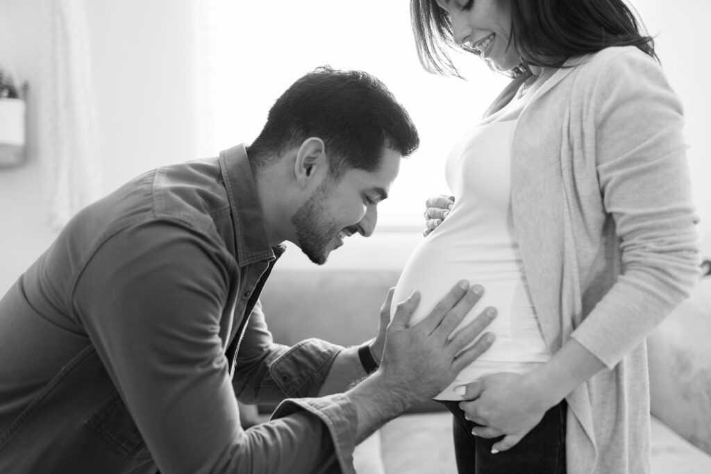 Expecting father smiling as he gently holds his partner's pregnant belly