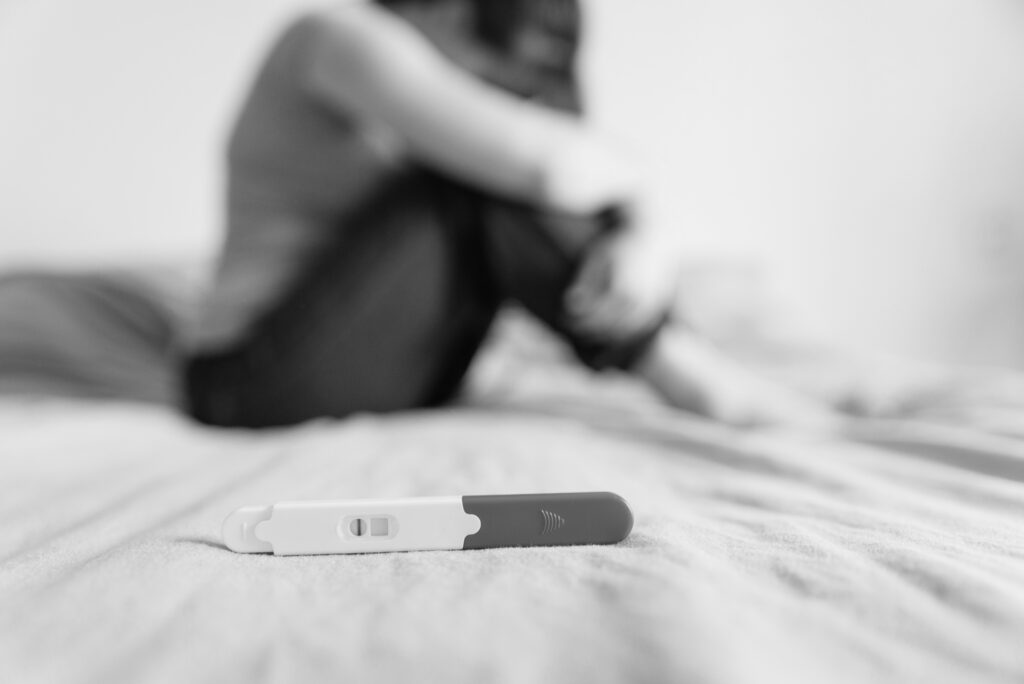 Close-up of a negative pregnancy test with a sad woman sitting in the background