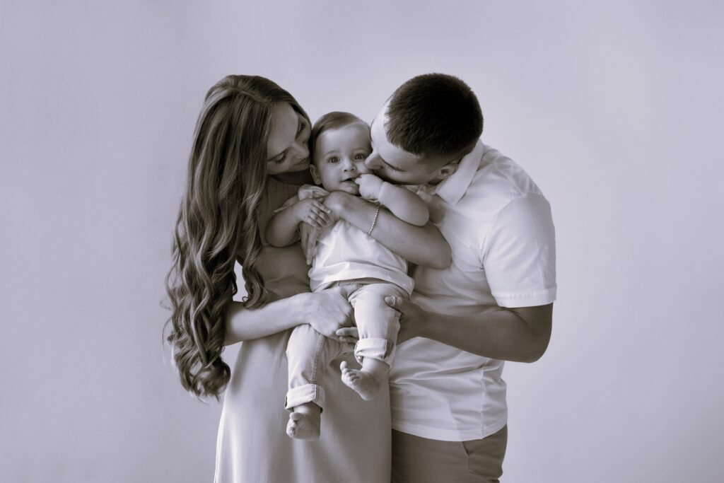 Happy young family. Beautiful Mother and father kissing their baby. Parents, Portrait of Mom, dad and smiling child on hands isolated over white background.
