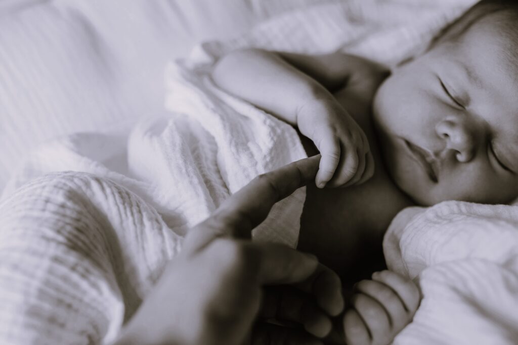 Closeup of a newborn baby holding mother's finger.