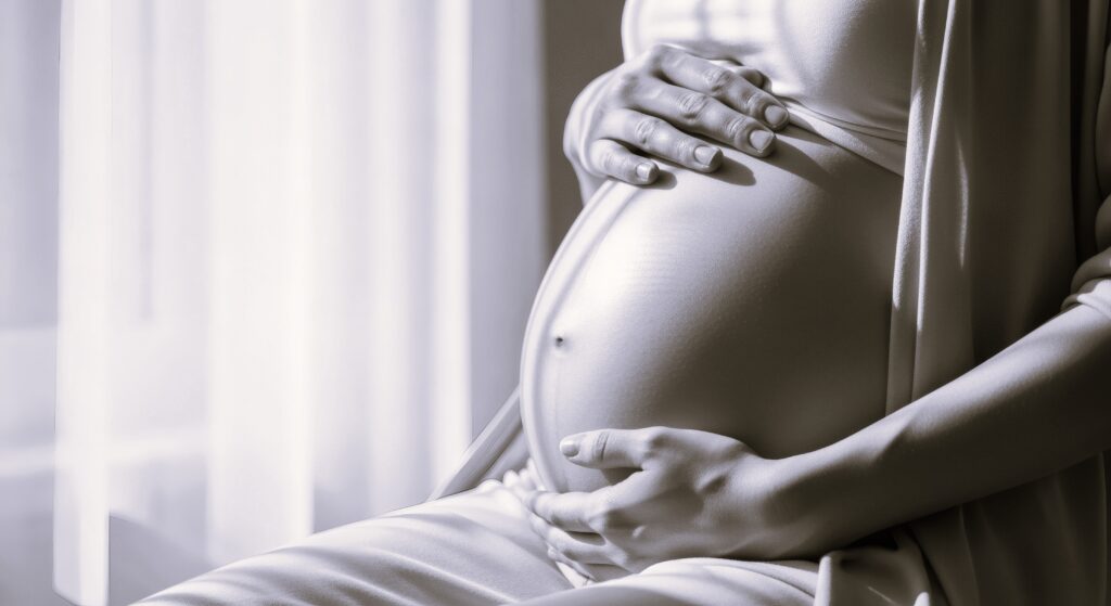 A close-up of a woman holding her pregnant belly, her baby bump