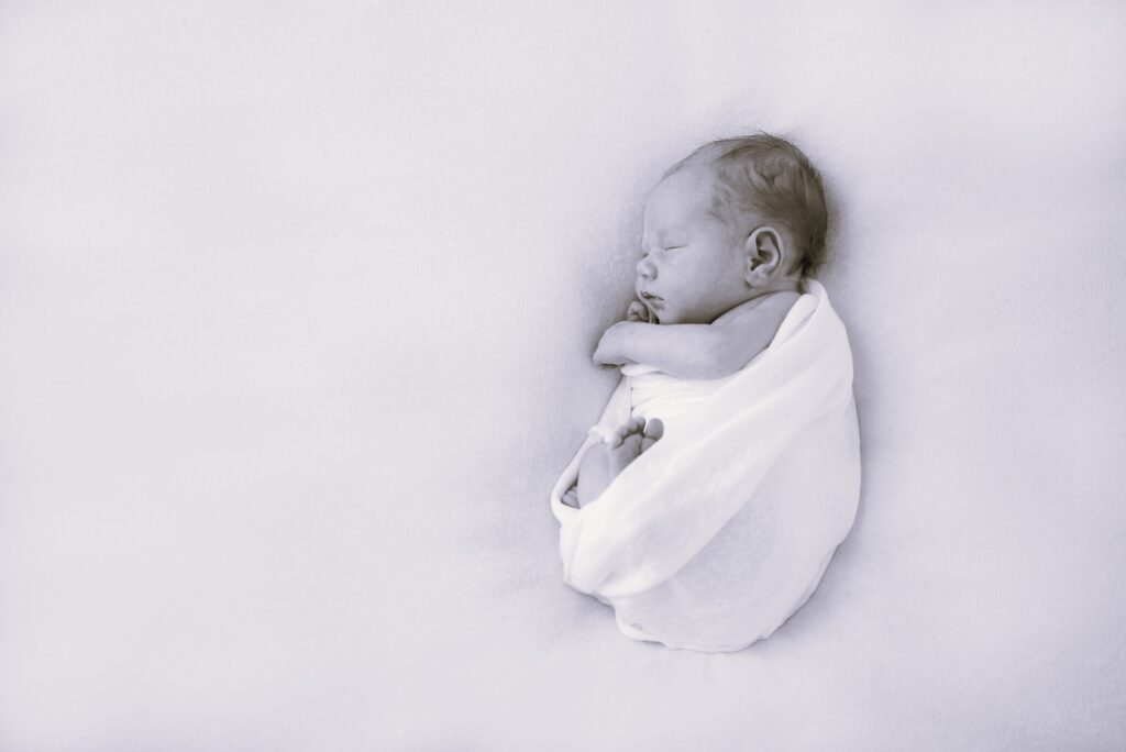Cute newborn baby lies swaddled in a white blanket laying on another white blanket.