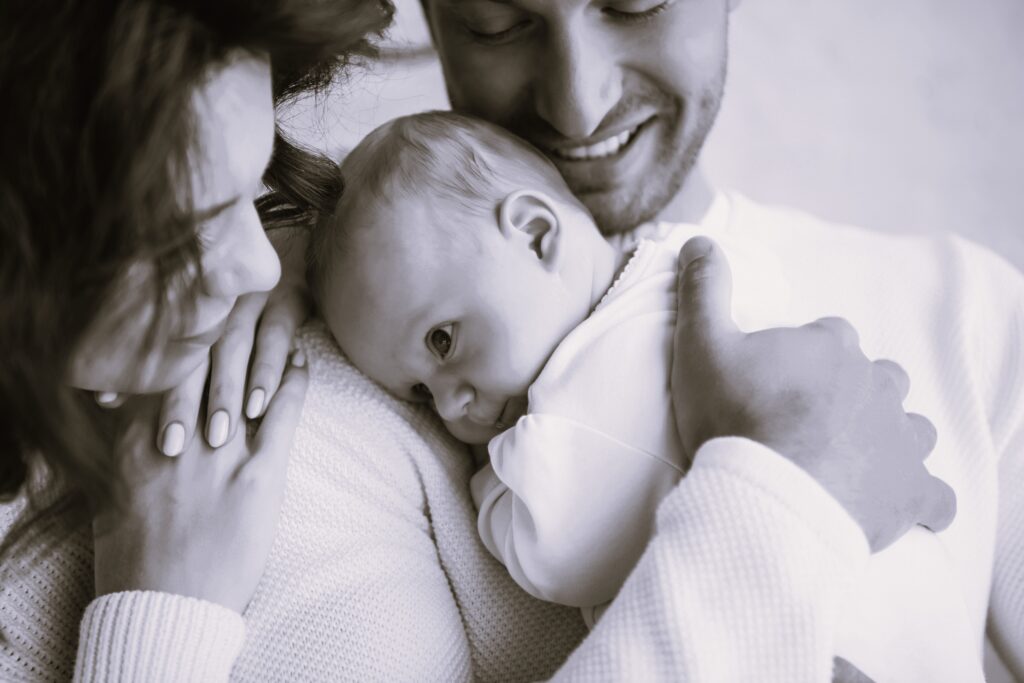 A cropped view of happy man holding adorable baby near smiling wife, while they both smile happily at their baby.